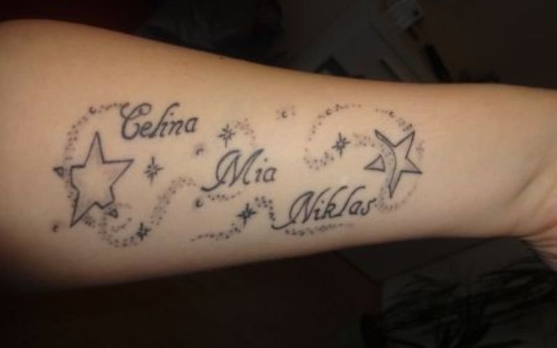 A forearm tattoo featuring the names Celina, Mia, and Niklas in cursive script, surrounded by stars and dotted swirling lines.