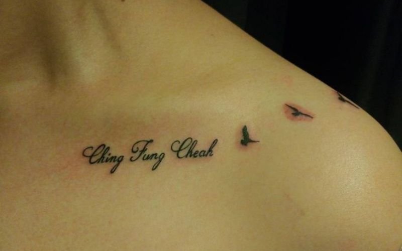 A tattoo on a persons upper chest features the words Stay Free Cheat in cursive script, with two small black bird silhouettes flying nearby.