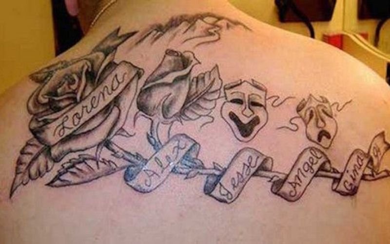 A tattoo on a persons upper back features roses, theater masks, and a ribbon with the names: Lorena, Alex, Jesse, Angel, and Cristina written on it.