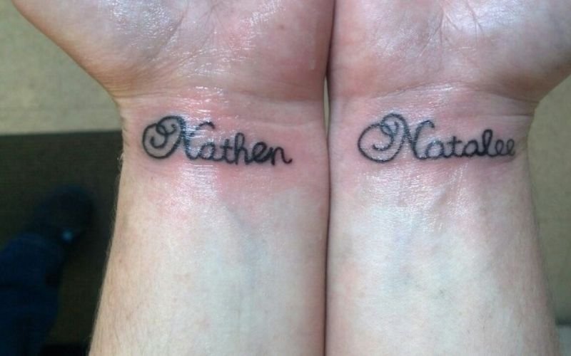 Two wrists with fresh tattoos in cursive script; the left wrist reads Nathan and the right wrist reads Natalie. The skin around the tattoos appears slightly red.